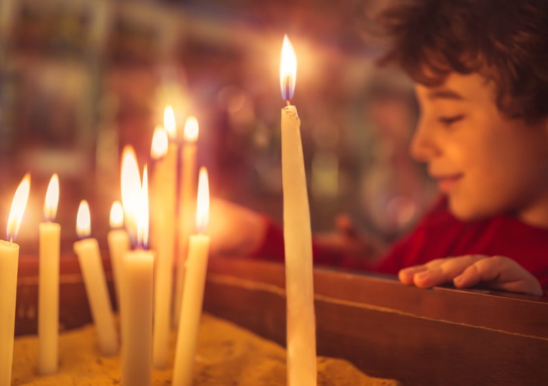 Little boy in the church on Easter, puts a candle to prays to God, enjoying happy religious holiday, good peaceful atmosphere in holy place